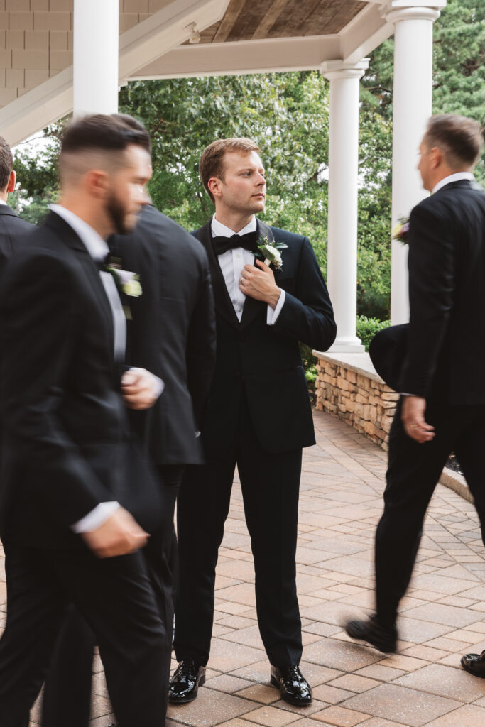Portrait of groom holding his jacket and looking off to the side as his groomsmen walk around him in an aesthetic blur, photographed by Philadelphia and New Jersey based travel wedding photographer, Madison Neumann Photography.