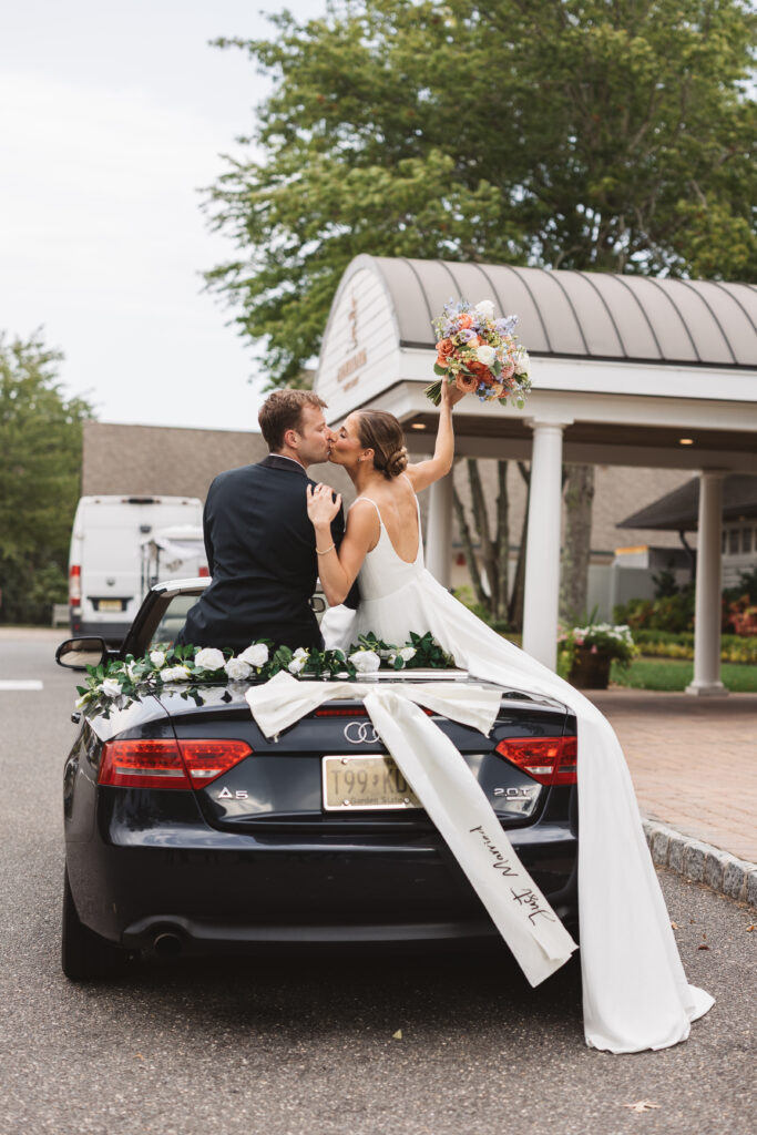 Bride and groom kiss on the back of an Audi convertible with a 'just married' bow and flowers on the back, photographed by Philadelphia and New Jersey based travel wedding photographer, Madison Neumann Photography.