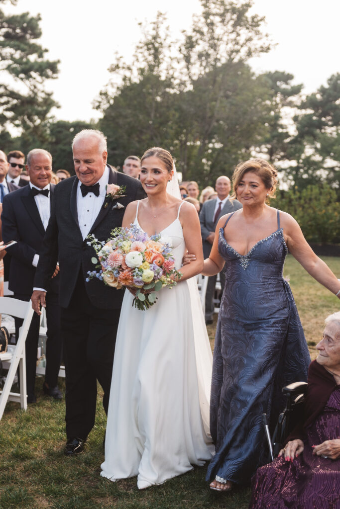 Bride being walked down the aisle by her parents with an excited smile on her face, photographed by Philadelphia and New Jersey based travel wedding photographer, Madison Neumann Photography.