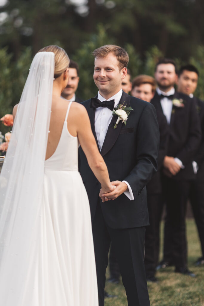 Bride and groom at the altar shot from behind the bride as we see a smiling groom and a beautiful veil with pearl detailing, photographed by Philadelphia and New Jersey based travel wedding photographer, Madison Neumann Photography.