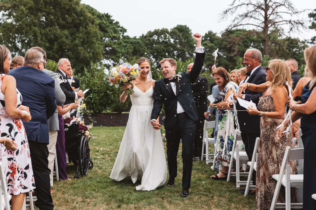 Bride and groom holding their hands high as they exit the ceremony with confetti surrounding them, photographed by Philadelphia and New Jersey based travel wedding photographer, Madison Neumann Photography.