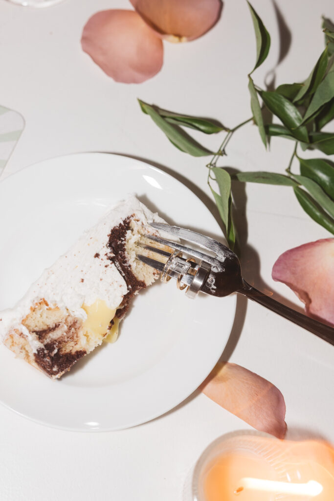Closing detail shot of fork in the wedding cake with the wedding rings on it featuring a simple but elegant emerald cut engagement ring, photographed by Philadelphia and New Jersey based travel wedding photographer, Madison Neumann Photography.